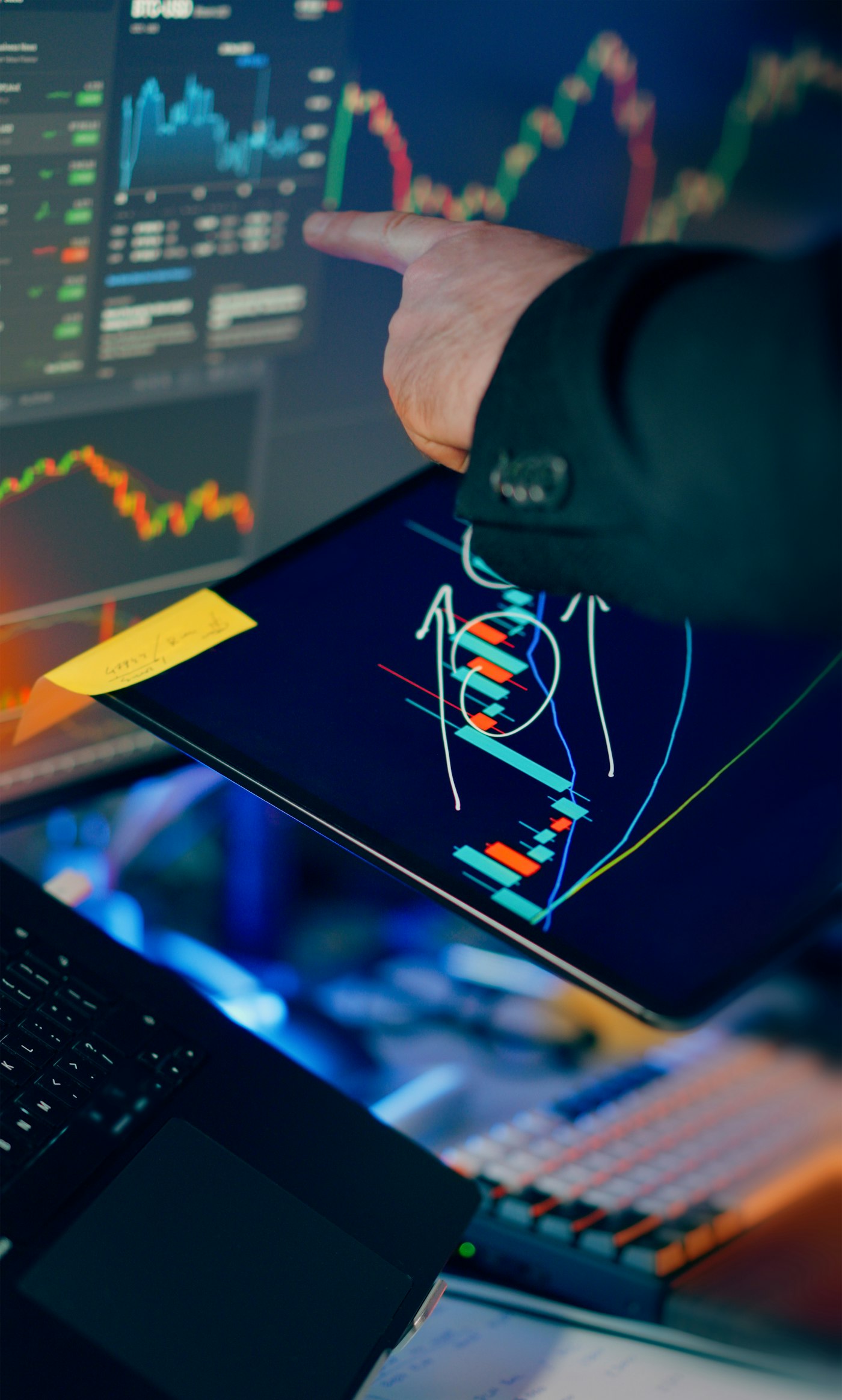 A trader studying candlestick charts across a monitor and tablet